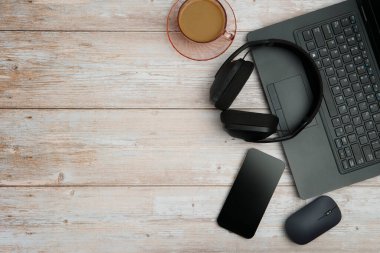 Bilgisayarlı, akıllı telefonlu, fareli, kulaklıklı ve beyaz ahşap masadaki kahve ile en üst düzey çalışma alanı üretkenliği, uzaktan çalışmayı, dijital odağı ve temiz kopya alanı olan profesyonel ofis ortamını temsil ediyor..