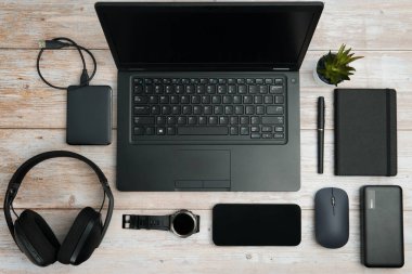 Dizüstü bilgisayarı, akıllı telefonu, kulaklığı, faresi, defteri, saati ve aksesuarları olan düz çalışma alanı üretkenliği, uzaktan çalışmayı ve dijital profesyonel yaşam tarzını temsil eden beyaz ahşap masa üzerindeki aksesuarlar..