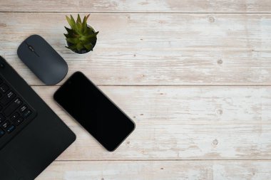 Üst görünüm minimal iş alanı dizüstü bilgisayarı, akıllı telefonu, faresi ve beyaz ahşap masa üzerine bitkisi ile verimliliği temsil eden, dijital çalışma ortamı, ve temiz kopya alanı ile profesyonel ofis kurulumu.