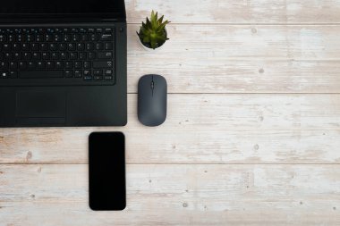 Üst görünüm minimal iş alanı dizüstü bilgisayarı, akıllı telefonu, faresi ve beyaz ahşap masa üzerine bitkisi ile verimliliği temsil eden, dijital çalışma ortamı, ve temiz kopya alanı ile profesyonel ofis kurulumu.