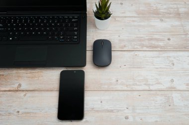 Üst görünüm minimal iş alanı dizüstü bilgisayarı, akıllı telefonu, faresi ve beyaz ahşap masa üzerine bitkisi ile verimliliği temsil eden, dijital çalışma ortamı, ve temiz kopya alanı ile profesyonel ofis kurulumu.