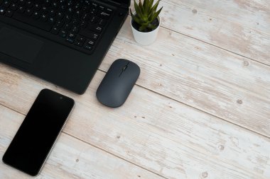 Üst görünüm minimal iş alanı dizüstü bilgisayarı, akıllı telefonu, faresi ve beyaz ahşap masa üzerine bitkisi ile verimliliği temsil eden, dijital çalışma ortamı, ve temiz kopya alanı ile profesyonel ofis kurulumu.