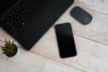 Üst görünüm minimal iş alanı dizüstü bilgisayarı, akıllı telefonu, faresi ve beyaz ahşap masa üzerine bitkisi ile verimliliği temsil eden, dijital çalışma ortamı, ve temiz kopya alanı ile profesyonel ofis kurulumu.