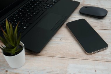 Üst görünüm minimal iş alanı dizüstü bilgisayarı, akıllı telefonu, faresi ve beyaz ahşap masa üzerine bitkisi ile verimliliği temsil eden, dijital çalışma ortamı, ve temiz kopya alanı ile profesyonel ofis kurulumu.