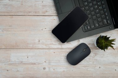 Üst görünüm minimal iş alanı dizüstü bilgisayarı, akıllı telefonu, faresi ve beyaz ahşap masa üzerine bitkisi ile verimliliği temsil eden, dijital çalışma ortamı, ve temiz kopya alanı ile profesyonel ofis kurulumu.