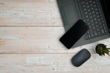 Üst görünüm minimal iş alanı dizüstü bilgisayarı, akıllı telefonu, faresi ve beyaz ahşap masa üzerine bitkisi ile verimliliği temsil eden, dijital çalışma ortamı, ve temiz kopya alanı ile profesyonel ofis kurulumu.