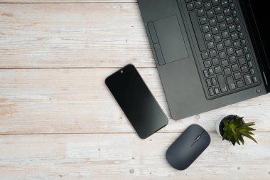 Üst görünüm minimal iş alanı dizüstü bilgisayarı, akıllı telefonu, faresi ve beyaz ahşap masa üzerine bitkisi ile verimliliği temsil eden, dijital çalışma ortamı, ve temiz kopya alanı ile profesyonel ofis kurulumu.