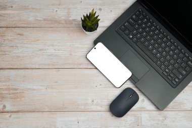 Üst görünüm iş alanı dizüstü bilgisayarı, boş akıllı telefonu, faresi ve beyaz ahşap masa üzerine bitkisi verimliliği, dijital işi, model görüntüsünü ve temiz kopya alanı olan profesyonel ofis kurulumunu temsil ediyor..