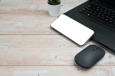 Üst görünüm iş alanı dizüstü bilgisayarı, boş akıllı telefonu, faresi ve beyaz ahşap masa üzerine bitkisi verimliliği, dijital işi, model görüntüsünü ve temiz kopya alanı olan profesyonel ofis kurulumunu temsil ediyor..
