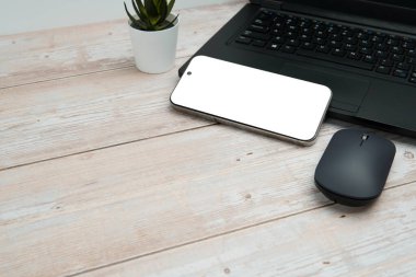 Üst görünüm iş alanı dizüstü bilgisayarı, boş akıllı telefonu, faresi ve beyaz ahşap masa üzerine bitkisi verimliliği, dijital işi, model görüntüsünü ve temiz kopya alanı olan profesyonel ofis kurulumunu temsil ediyor..