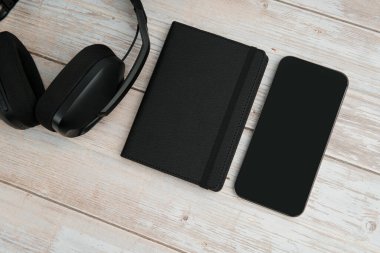 Kulaklık, not defteri ve beyaz ahşap arka planda boş akıllı telefon modern çalışma alanını temsil eden dijital yaşam tarzı, verimlilik, uzaktan çalışma ve fotokopi alanı ile minimal iş ayarları..