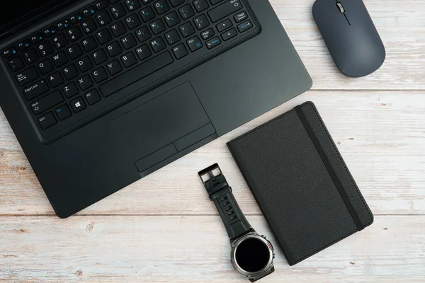 Üst görünüm iş alanı dizüstü bilgisayarı, fare, not defteri ve beyaz ahşap masa üzerindeki kol saati üretkenliği, zaman yönetimini, dijital çalışmayı ve temiz kopya alanı olan profesyonel ofis düzeneğini temsil ediyor..