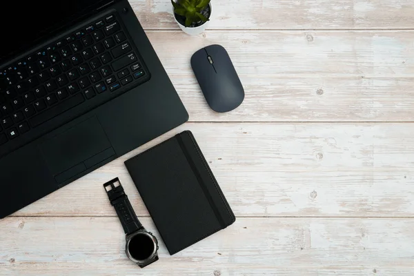 Üst görünüm iş alanı dizüstü bilgisayarı, fare, not defteri ve beyaz ahşap masa üzerindeki kol saati üretkenliği, zaman yönetimini, dijital çalışmayı ve temiz kopya alanı olan profesyonel ofis düzeneğini temsil ediyor..