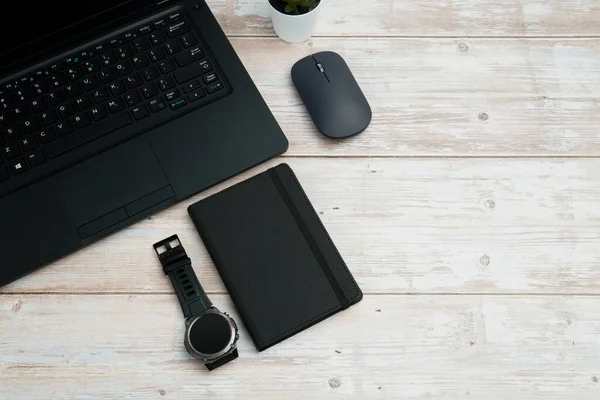 Üst görünüm iş alanı dizüstü bilgisayarı, fare, not defteri ve beyaz ahşap masa üzerindeki kol saati üretkenliği, zaman yönetimini, dijital çalışmayı ve temiz kopya alanı olan profesyonel ofis düzeneğini temsil ediyor..