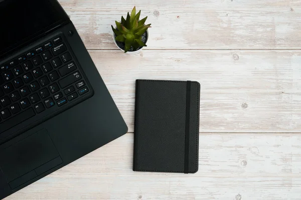 Verimliliği, planlamayı, dijital çalışma ortamını ve temiz fotokopi alanı olan profesyonel ofis ortamını temsil eden dizüstü bilgisayarlı, defterli ve beyaz ahşap masa üzerindeki işletme çalışma alanının en üst görünümü.