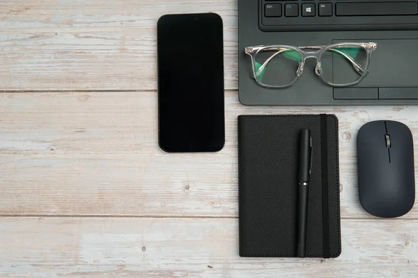 Dizüstü bilgisayarlı, akıllı telefonlu, gözlüklü, defterli ve fareli en iyi iş yeri beyaz ahşap masadaki verimliliği, dijital çalışmayı ve temiz kopya alanı olan profesyonel ofis ortamını temsil ediyor..