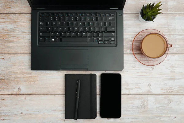 Bilgisayarlı, akıllı telefonlu, not defterli ve beyaz ahşap masadaki kahve fincanı ile en üst düzey çalışma alanı üretkenliği, dijital işi, günlük rutini ve temiz kopya alanı olan profesyonel ofis düzenini temsil ediyor..