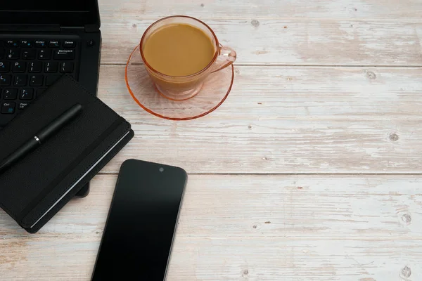 Bilgisayarlı, akıllı telefonlu, not defterli ve beyaz ahşap masadaki kahve fincanı ile en üst düzey çalışma alanı üretkenliği, dijital işi, günlük rutini ve temiz kopya alanı olan profesyonel ofis düzenini temsil ediyor..