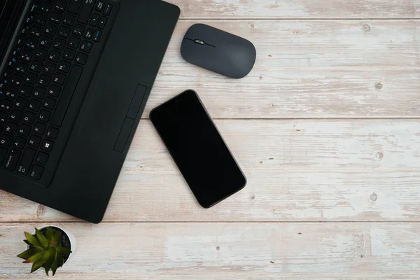 Üst görünüm minimal iş alanı dizüstü bilgisayarı, akıllı telefonu, faresi ve beyaz ahşap masa üzerine bitkisi ile verimliliği temsil eden, dijital çalışma ortamı, ve temiz kopya alanı ile profesyonel ofis kurulumu.