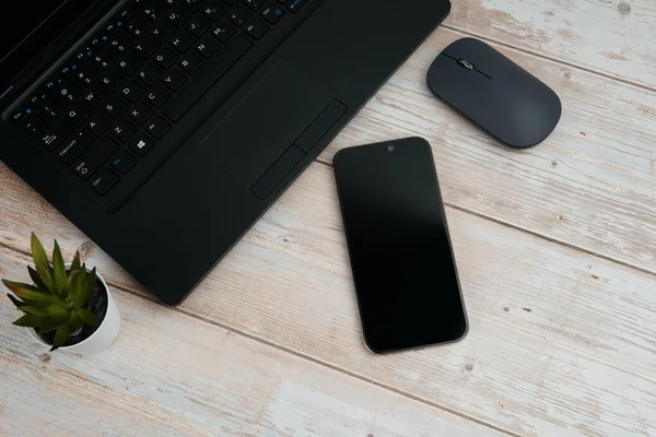 Üst görünüm minimal iş alanı dizüstü bilgisayarı, akıllı telefonu, faresi ve beyaz ahşap masa üzerine bitkisi ile verimliliği temsil eden, dijital çalışma ortamı, ve temiz kopya alanı ile profesyonel ofis kurulumu.