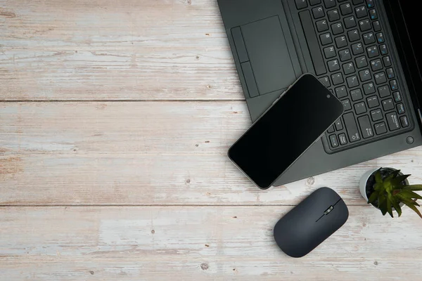 Üst görünüm minimal iş alanı dizüstü bilgisayarı, akıllı telefonu, faresi ve beyaz ahşap masa üzerine bitkisi ile verimliliği temsil eden, dijital çalışma ortamı, ve temiz kopya alanı ile profesyonel ofis kurulumu.