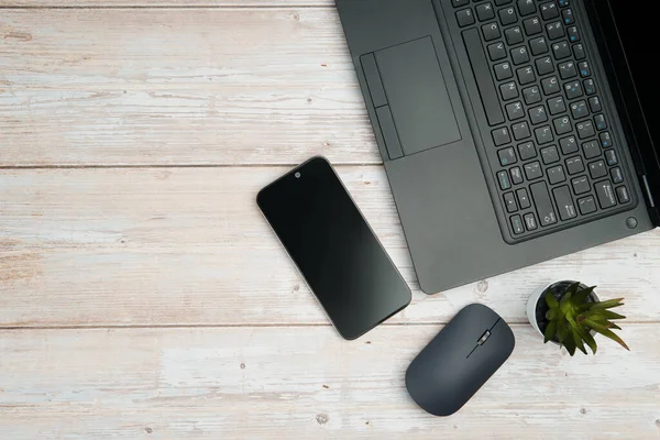Üst görünüm minimal iş alanı dizüstü bilgisayarı, akıllı telefonu, faresi ve beyaz ahşap masa üzerine bitkisi ile verimliliği temsil eden, dijital çalışma ortamı, ve temiz kopya alanı ile profesyonel ofis kurulumu.