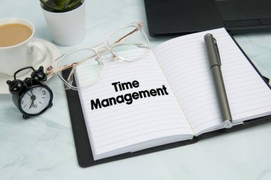 Zaman Yönetimi 'ni, kalemi, çalar saati, kahve fincanını, bardakları ve dizüstü bilgisayarını gösteren açık not defteriyle üst kattaki ofis çalışma alanı. Üretkenlik, verimlilik, planlama ve profesyonel zaman kontrolü kavramı