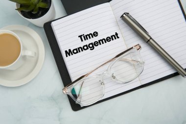 Zaman Yönetimi 'ni, kalemi, çalar saati, kahve fincanını, bardakları ve dizüstü bilgisayarını gösteren açık not defteriyle üst kattaki ofis çalışma alanı. Üretkenlik, planlama ve profesyonel zaman kontrolü kavramı.