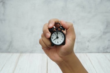 Elinde zaman yönetimi ve aciliyeti simgeleyen küçük bir çalar saat var..