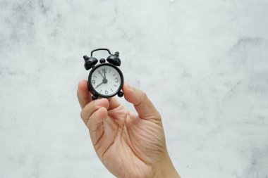 Elinde zaman yönetimi ve aciliyeti simgeleyen küçük bir çalar saat var..