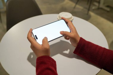 Eller servis tabağının yanında boş beyaz ekranlı akıllı telefon kullanıyor, mobil teknolojiyi, uygulama kullanımını, dijital etkileşimi, çevrimiçi iletişimi ve modern yaşam tarzı kavramını sembolize ediyor.