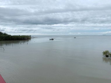 Kayalar, sığ deniz ve bulutlu gökyüzü ile sakin kıyı şeridi, doğal deniz manzarasını, kıyı ortamını, huzurlu suları ve açık hava manzarasını temsil eder..