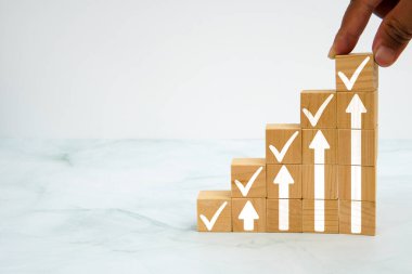 Elle tahta bloğu yukarı doğru ok ve kontrol işaretleri ile yerleştirmek, iş büyümesi ve mermer arka planda başarı kavramı.