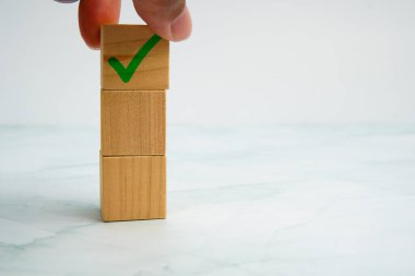 Yığının üzerine yeşil onay işareti olan ahşap küpün yerleştirilmesi, görev tamamlama ve iş onayı kavramını sembolize ediyor.
