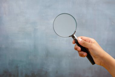 Hand holding magnifying glass on blue background, representing risk management, inspection and business analysis concept.