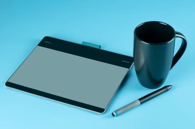 Grafik tasarımcılarının çalışma yeri veya çalışma alanı, dijital kalemli küçük grafik tableti ve Cyan çalışma alanında izole edilmiş siyah kahve fincanı.