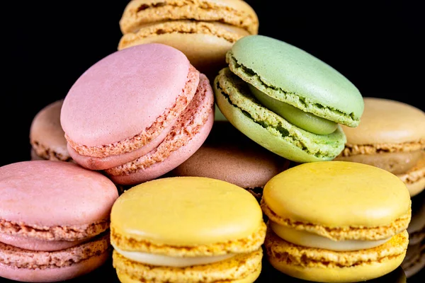 Close-up of French dessert for coffee. Multicolored macarons on black background.