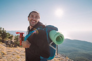 Yürüyüş yapan bir adam şafak vakti bir dağın tepesinde termostan çay içer. Turist ekipmanlı genç adam neşe içinde sabah güneşiyle denize bakan dağlarda buluşuyor.