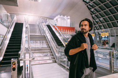 Havaalanındaki yürüyen merdivenin yanında bir adam var. Sırt çantalı genç bir adam terminalden uçağa biniyor.