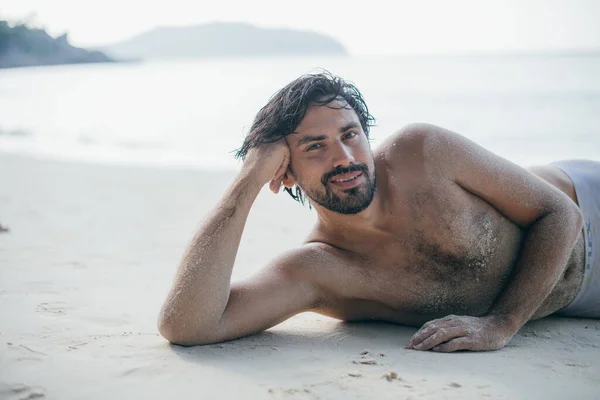 ハンサムな男が海のそばの砂の上に横たわっている 若い男 モデルは 熱帯のビーチで裸の胴とポーズ セクシーな筋肉質の男 肖像画 — ストック写真