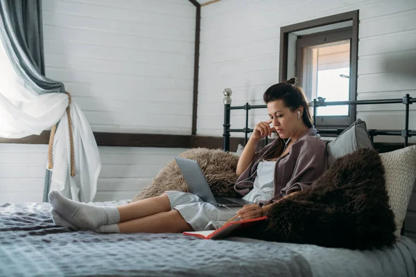 Woman works with laptop on the bed in the bedroom. A young girl lies on a large bed at home, works online, learns the language, communicates with clients