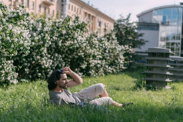 Homem Senta Grama Parque Florescendo Uma Cidade Grande Jovem Branco — Fotografia de Stock