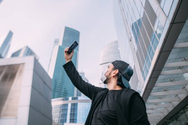 Issız bir şehirde elinde telefon olan bir adam. Genç bir adam, boş bir metropoldeki akıllı telefondan gökdelenleri alıyor.