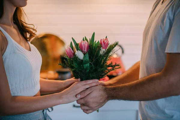 International Women\'s Day. Young couple in the morning in the kitchen at home. A man gives a woman a bouquet of tulips on March 8 in a beautiful stylish kitchen.