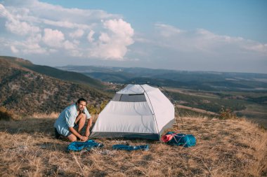 Genç erkek turist dağlara çadır kurdu. Adam yürüyüş için kamp kurmuş, gün batımında dağlarda tek başına çadır kurmuş.