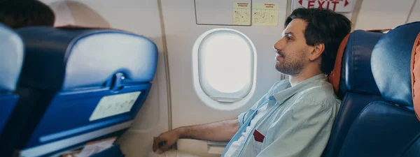 The guy is flying in an airplane. A young man is sitting in the seat of the plane during the flight.