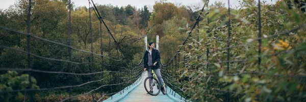 A man on a bicycle in the autumn on the bridge. Young guy with a bicycle on a large suspension bridge on an autumn day