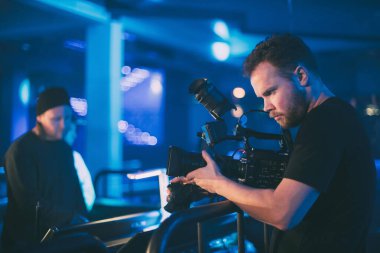 Görüntü yönetmeni elinde kamerayla sette. Bir film, ticari ya da televizyon dizisi çekmek için çalışan profesyonel bir videograf. İçerideki çekim süreci, neon lambalı bir konser sahnesinde..