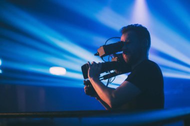 Görüntü yönetmeni elinde kamerayla sette. Bir film, ticari ya da televizyon dizisi çekmek için çalışan profesyonel bir videograf. İçerideki çekim süreci, neon lambalı bir konser sahnesinde..