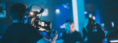 Görüntü yönetmeni elinde kamerayla sette. Bir film, ticari ya da televizyon dizisi çekmek için çalışan profesyonel bir videograf. İçerideki çekim süreci, neon lambalı bir konser sahnesinde..